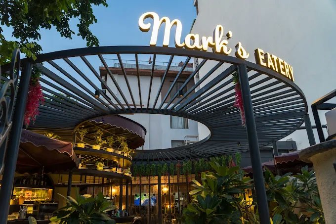 Mark’s Eatery at dusk, the sign lit beneath the steel pergola