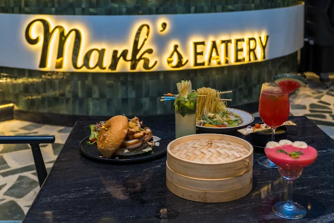 A table laid for sharing beneath the lit Mark’s Eatery sign